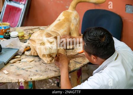 Ein Kunsthandwerker sandet ein großes Alebrije jaguar Spirituosentier, bevor er in einer Werkstatt in San Martin Tilcajete, Oaxaca, Mexiko malt. Stockfoto