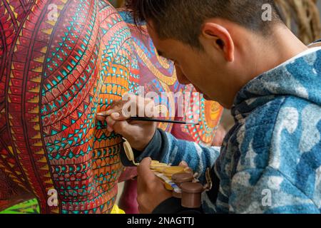 Ein Kunsthandwerker malt in einer Werkstatt in San Martin Tilcajete, Oaxaca, Mexiko, zapotekische Entwürfe auf einem alebrije-Spirituosentier. Stockfoto