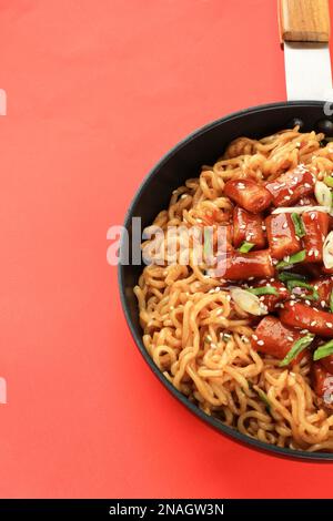 Rabokki, Koreanisches Street Food. Tteokbokki Topokki mit Instant Ramen auf der Pfanne, über dem roten Tisch Stockfoto