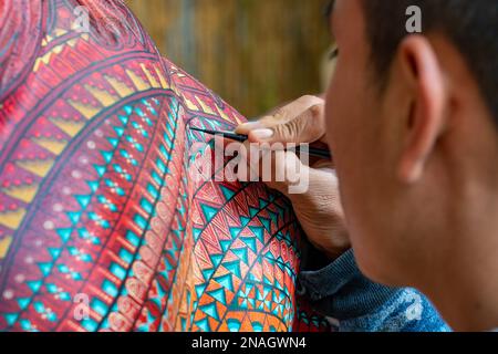 Ein Kunsthandwerker malt in einer Werkstatt in San Martin Tilcajete, Oaxaca, Mexiko, zapotekische Entwürfe auf einem alebrije-Spirituosentier. Stockfoto