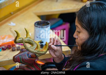 Ein Kunsthandwerker malt in einer Werkstatt in San Martin Tilcajete, Oaxaca, Mexiko, zapotekische Entwürfe auf einem alebrije-Spirituosentier. Stockfoto