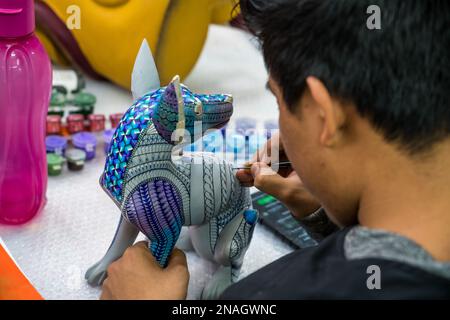 Ein Kunsthandwerker malt in einer Werkstatt in San Martin Tilcajete, Oaxaca, Mexiko, zapotekische Entwürfe auf einem alebrije-Spirituosentier. Stockfoto