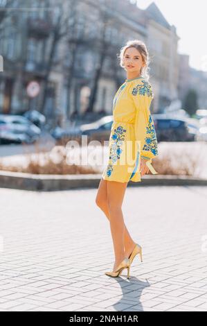 Ein junges Mädchen in einem traditionellen gelben Kleid auf der Straße. Ukrainerin in einem bestickten Kleid Stockfoto