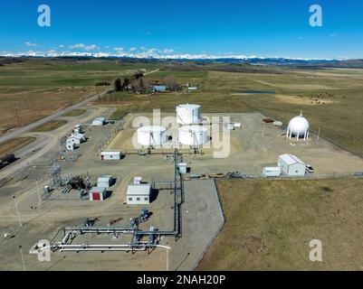 Aus der Vogelperspektive der großen runden Metallöllagertanks mit Pipelines, die sie mit dem blauen Himmel und den Bergen am Horizont verbinden, nördlich von Longview, Al... Stockfoto