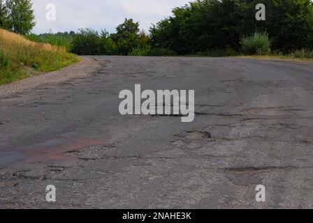 Ein Loch in der Straße. Gebrochener Asphalt. Zerstörte Oberfläche. Die Straße ist gerissen. Stockfoto