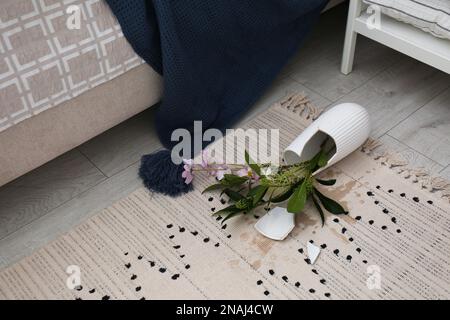 Zerbrochene Vase und Blumenstrauß auf dem Boden im Zimmer Stockfoto