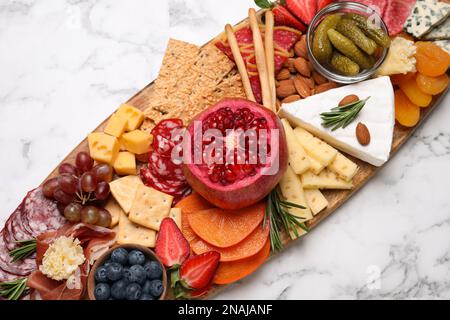 Holzteller mit verschiedenen leckeren Snacks auf weißem Marmortisch, Blick von oben Stockfoto