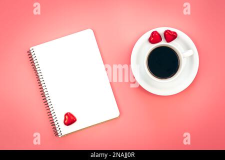Eine Tasse Kaffee, ein unbeschriftetes Notizbuch und herzförmige Süßigkeiten, Draufsicht. Stockfoto
