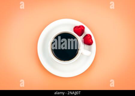 Tasse Kaffee und herzförmige Süßigkeiten auf orangefarbenem Hintergrund, flach liegend. Stockfoto