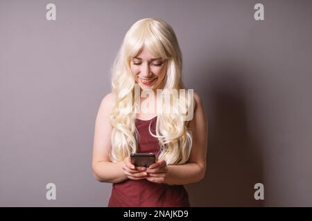 Fröhliche lächelnde junge Frau, die auf die Textnachricht herabschaut Ihr Smartphone - Mobile Kommunikation und Social Media Konzept Stockfoto