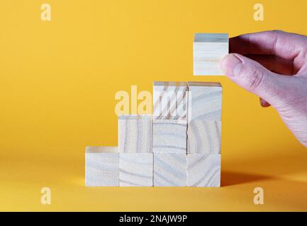 Nahaufnahme von Hand stapelbaren hölzernen Spielzeugblöcken in Treppenform vor orangefarbenem Hintergrund, Wachstum oder Leiter des Erfolgs Konzept Stockfoto