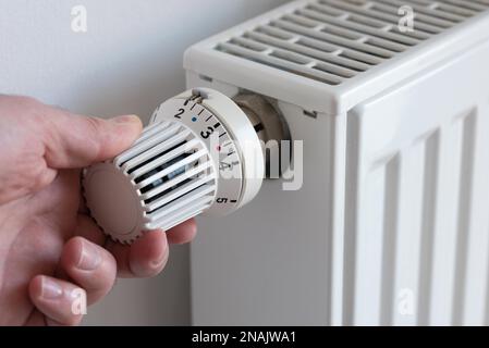 Nahaufnahme einer Person, die den Thermostat auf der Heizung herunterdreht, um zu sparen Energie Stockfoto