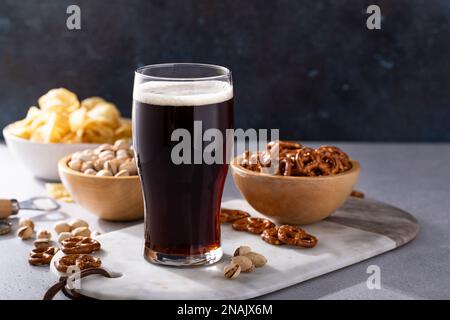 Dunkles, kräftiges Bier in einem hohen Glas, Bier und Snacks auf dem Tisch Stockfoto