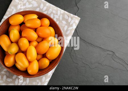 Frische reife Kumquats in Schüssel auf schwarzem Tisch, Draufsicht. Platz für Text Stockfoto