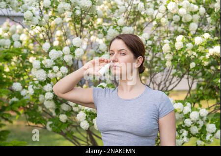 Kaukasische Frau verwendet ein Nasenspray, während sie im Park spazieren geht. Stockfoto