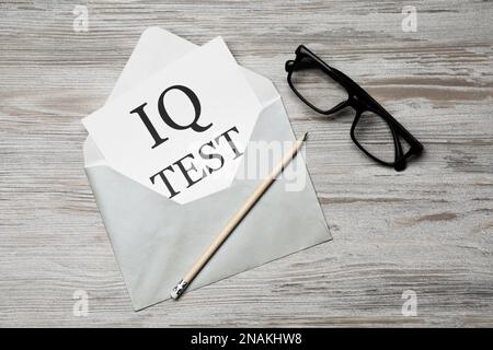 Papier mit den Worten IQ Test in Umschlag, Bleistift und Brille auf Holztisch, flach liegend Stockfoto