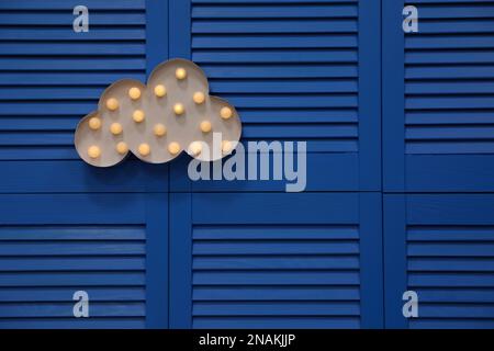 Stilvolle, wolkenförmige, leuchtende Nachtlampe, die auf einem blauen Klappbildschirm hängt. Platz für Text Stockfoto