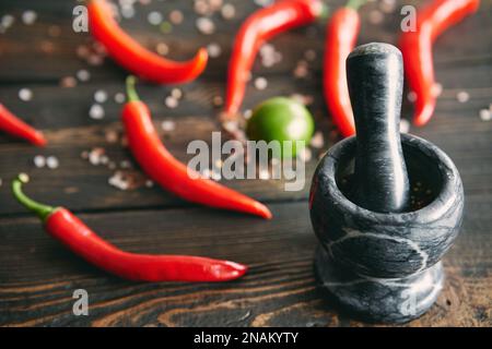Schwarzer Marmormörtel mit einem Pistill voll gemischter Pfefferkörner mit roter heißer Chili-Paprika auf dem Hintergrund. Gewürze zum Kochen, Styling-Konzept Stockfoto