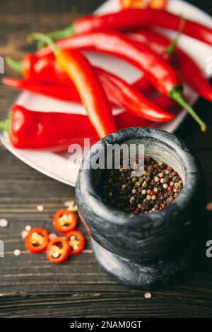 Schwarzer Marmormörtel mit einem Pistill voll gemischter Pfefferkörner mit roter heißer Chili-Paprika auf dem Hintergrund. Gewürze zum Kochen, Styling-Konzept Stockfoto