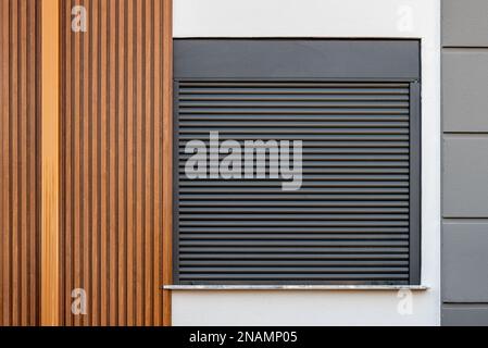 Das Gebäude, dessen Fassade mit holzgemusterten PVC-Paneelen bedeckt ist und dessen Fenster aus Fensterläden besteht Stockfoto