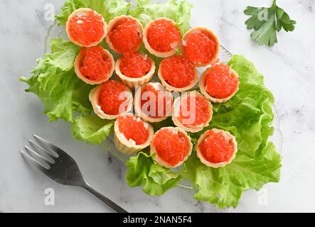 Törtchen mit Butter und rotem Kaviar. Teller mit Kaviar-Vorspeise, dekoriert mit Salatblättern auf hellem Hintergrund Stockfoto