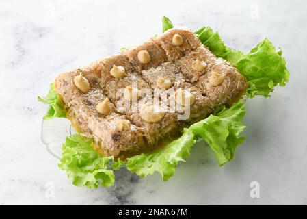 Schweinefleisch- und Rindfleischaspik, dekoriert mit Salatblättern auf einem Teller auf hellem Hintergrund. Fleischgelee Stockfoto