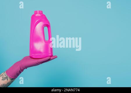 Zugeschnittene Ansicht eines tätowierten Mannes in Gummihandschuhen, der eine Flasche Waschgel hält, isoliert auf blauem Stammbild Stockfoto