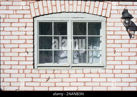 Altes Fenster in einem Ziegelhaus, Tulle-Vorhang und eine Laterne an der Wand Stockfoto