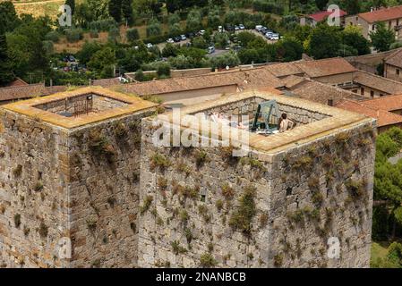 SAN GIMIGNANO, ITALIEN - 12. JULI 2014: Der obere Teil von zwei antiken Türmen mit ein paar Touristen in der Innenstadt von San Gimignano, mittelalterliche Stadt in Siena PR Stockfoto