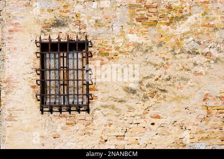 Detail eines Fensters mit einem alten und rostigen Gitter an einer alten Wand mit Ziegeln. San Gimignano, Siena, Toskana, Italien Stockfoto