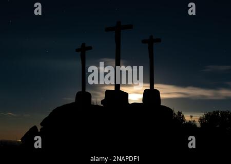 Drei Kreuze aus geschnitztem Stein auf Granitfelsen in der Dämmerung des Himmels. Stockfoto