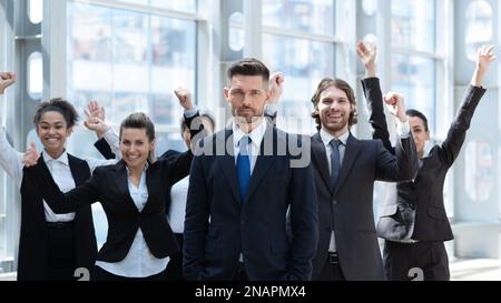 Team der Gewinner des Unternehmens. Gruppe von glücklichen Menschen in formeller Kleidung, die feiern, gestikulieren, die Arme hochhalten und Positivität ausdrücken Stockfoto