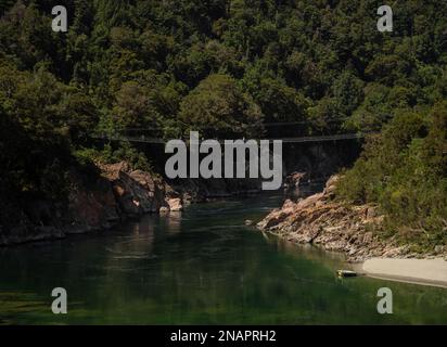 Blick auf den Fluss, bei dem mehrere Personen die längste Buller Gorge Swing Bridge überqueren, die sich über 110 m über den Buller River in Murchison Tasman South Island New Ze erstreckt Stockfoto