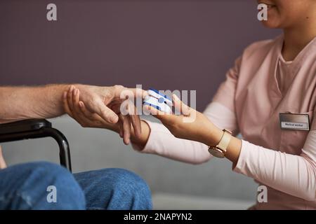 Nahaufnahme einer jungen Krankenschwester in Uniform, die Hand eines älteren Mannes hält und seinen Puls mit spezieller medizinischer Ausrüstung prüft Stockfoto