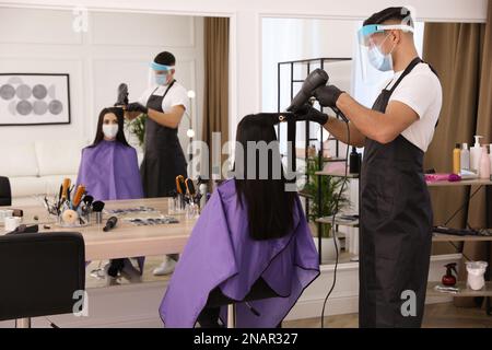 Professioneller Stylist, der mit einem Kunden im Salon zusammenarbeitet. Friseurdienste während der Coronavirus-Quarantäne Stockfoto