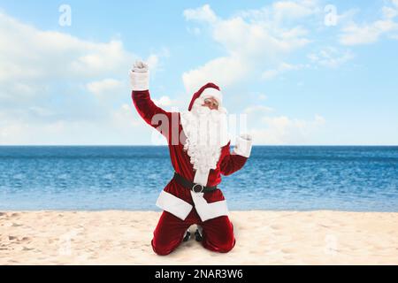 Fröhlicher Weihnachtsmann am Sandstrand in der Nähe des Meeres. Weihnachtsferien Stockfoto