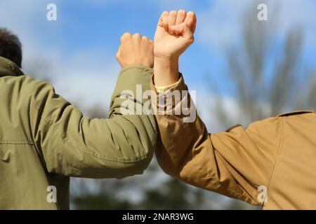 Die Leute grüßen sich gegenseitig, indem sie Ellbogen statt Handschlag im Freien anstoßen, Nahaufnahme Stockfoto