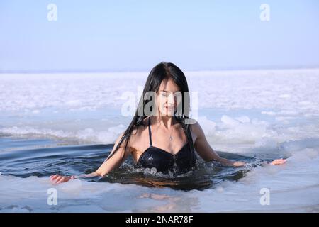 Frau, die am Wintertag in eiskaltes Wasser taucht. Taufe-Ritual Stockfoto