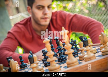 Schließen. Ein Mann, der Schach spielt, über den nächsten Zug nachdenkt, den Frühlingstag, draußen. Stockfoto