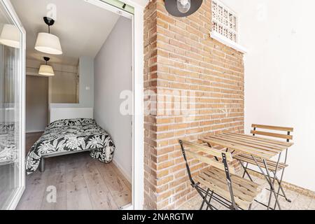 Schlafzimmer mit einem Einzelbett mit auffälliger Matratze, Kastanienboden und einer kleinen Terrasse mit Holztisch und zwei Klappstühlen Stockfoto