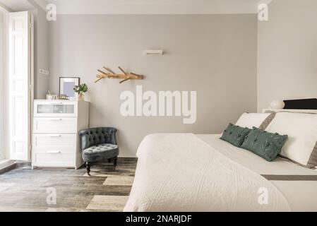 Schlafzimmer mit einem Doppelbett mit grünen Kissen und einer Kommode mit weißen Schubladen neben einem grün gepolsterten Sessel Stockfoto
