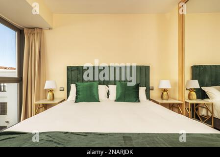 Schlafzimmer mit einem Doppelbett mit grünen Kissen und gepolstertem Kopfteil der gleichen Farbe neben einem Fenster Stockfoto