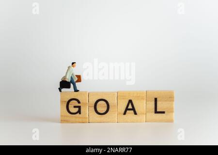 Business- und Reisekonzept. Geschäftsmann Miniaturfigur Personen mit Handtaschen Koffer laufen auf hölzernen Buchstabenblöcken Text Tor. Stockfoto