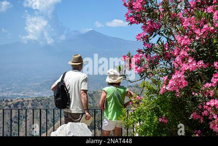 Älteres Paar, das den Ätna von einem wunderschönen, blühenden Aussichtspunkt aus im antiken Theater von Taormina, Sizilien, Italien beobachtet. Stockfoto