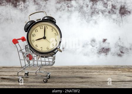Warenkorb mit Vintage-Wecker auf einem rustikalen Holztisch mit Platz für Text. Konzept des Verkaufs und saisonale Rabatte in den Geschäften. Stockfoto