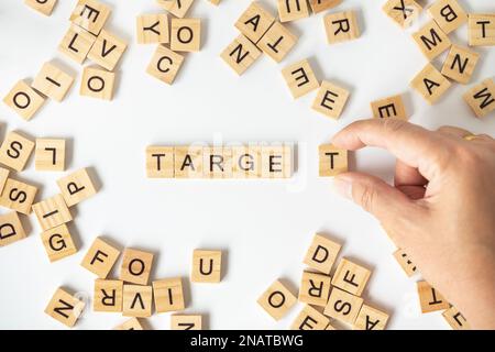 Geschäftskonzept. Nahaufnahme einer Hand, die einen hölzernen T-Buchstabenblock hält, um DEN ZIELTEXT mit anderen englischen Buchstabenblöcken auf weißem Hintergrund zu vervollständigen. Stockfoto