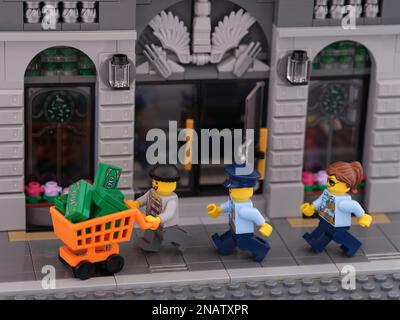 Tambov, Russische Föderation - 08. Februar 2023 Ein Lego-Dieb-Minifigure mit einem Einkaufswagen voller Geld, der vor zwei Polizisten Minifig wegläuft Stockfoto