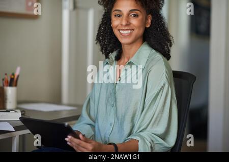 Lächelnde junge Geschäftsfrau, die in ihrem Heimbüro an einem Tablet arbeitet Stockfoto