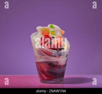 Gemischtes Obst mit Joghurt und Minze in einem Glasgericht mit abgestuftem Hintergrund. Stockfoto