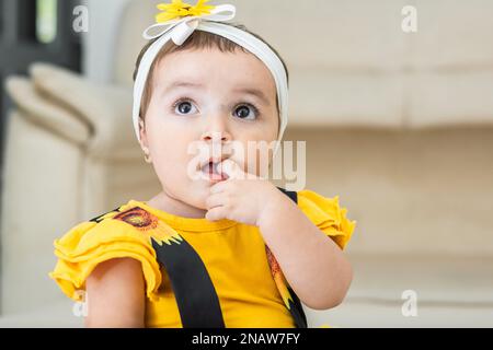 Wunderschönes Latina-Baby, das mit einem erstaunten Gesicht aufblickt, während es einen Finger in den Mund steckte. Stockfoto